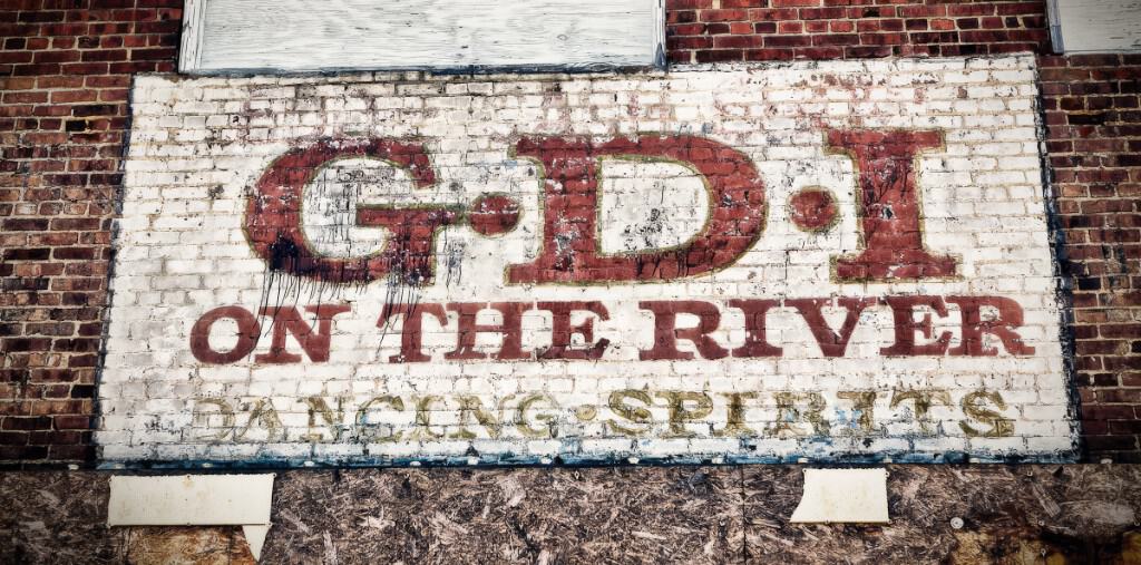 Weathered GDI on the River sign on brick — George's Disco Incorporated