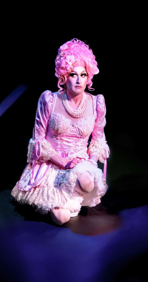 Performer in feathered gown and pink wig kneels on stage during Memphis show. — friendsofgeorges.org