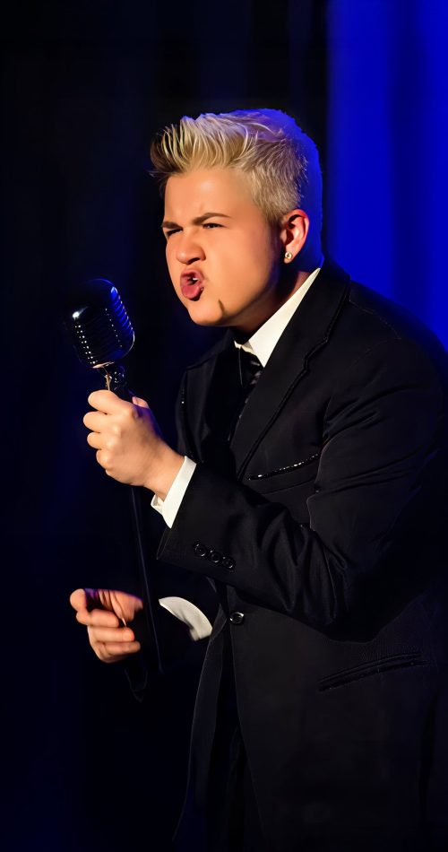 Performer in tuxedo sings passionately into a vintage microphone on stage. — friendsofgeorges.org